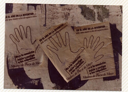 Campaña “Dele una mano a los desaparecidos", detalle de tres hojas-afiches de manos sobre muro urbano.